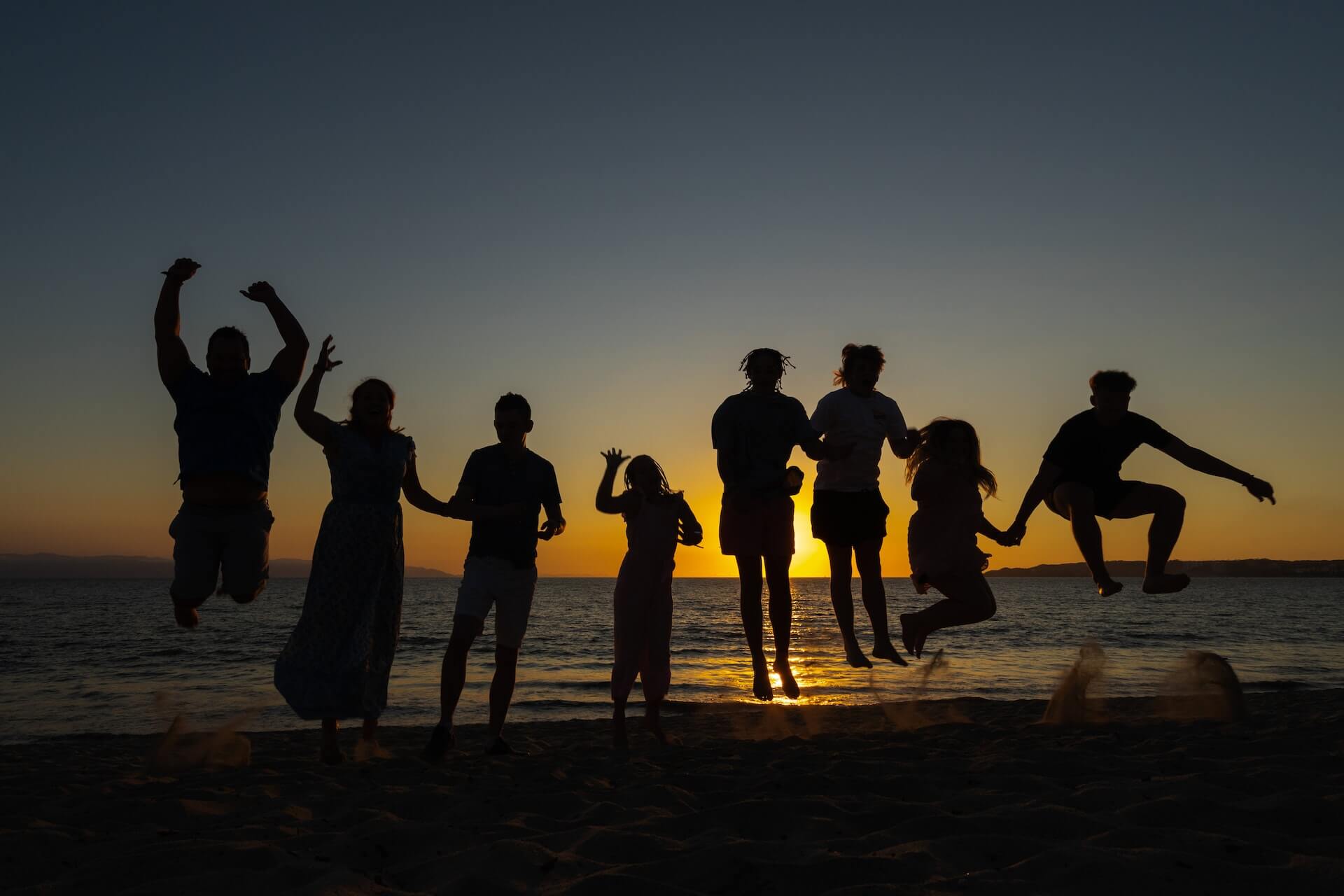 Image of a large family jumping together at the beach while the sun sets behind them